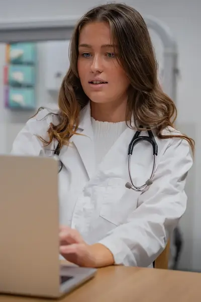 Student verpleegkunde in uniform achter laptop