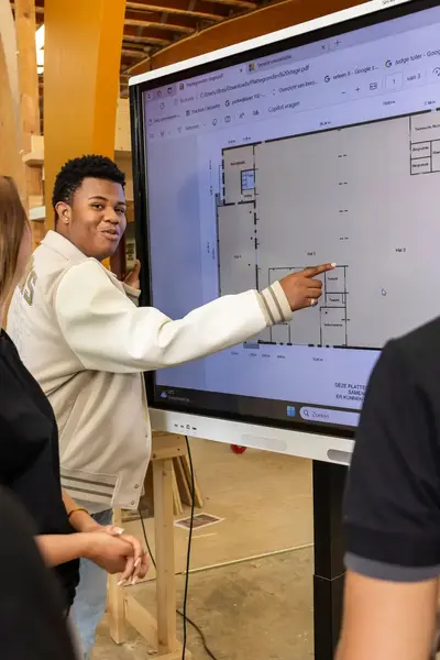 Studenten staan te kijken naar een groot digitaal scherm waarop een bouwtekening te zien is. 