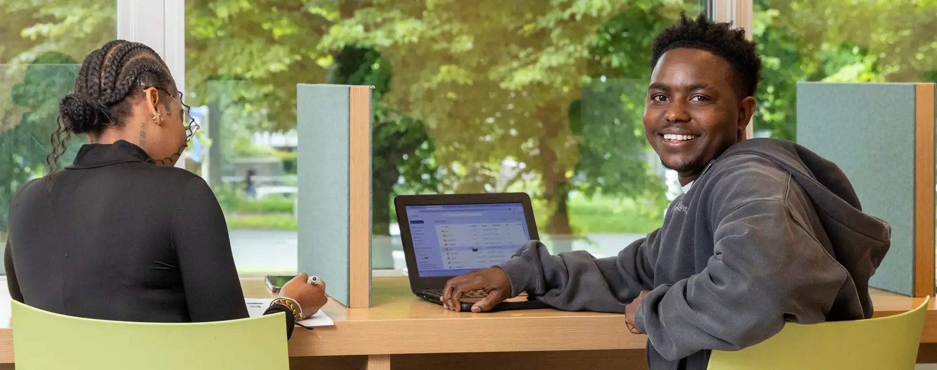 Student achter laptop voor raam op gele stoel