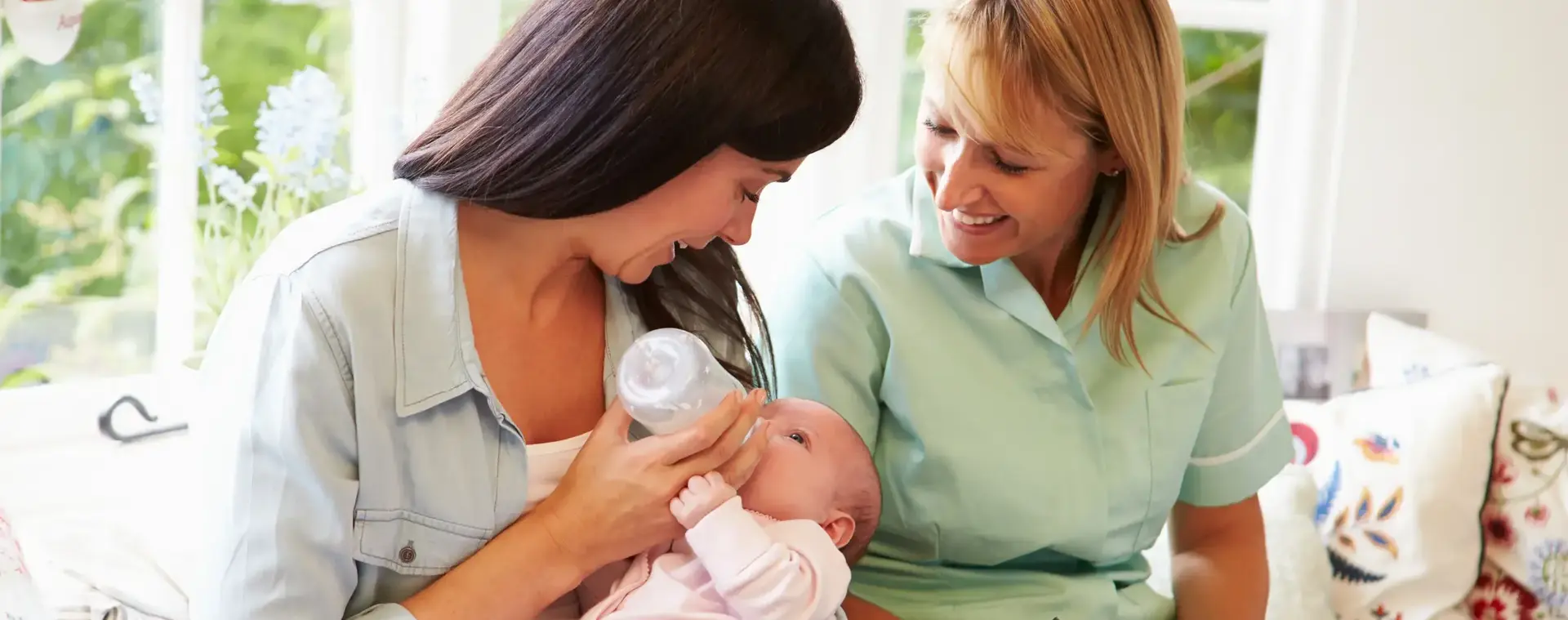 Kraamverzorgende naast vrouw die baby flesvoeding geeft