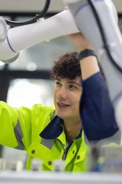 Student onderzoekt geconcentreerd een geavanceerde robotarm in een hightech omgeving. Hij draagt een fluorescerend werkjack en werkt nauwkeurig. 