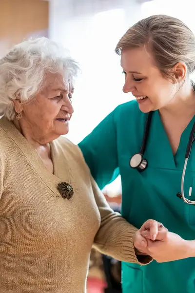 Verzorger ondersteunt oude dame.