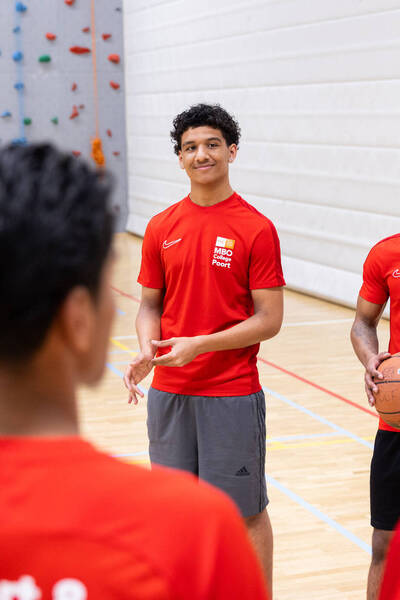 Sportstudenten in rood sporttenue in gymzaal tijdens basketbaltraining