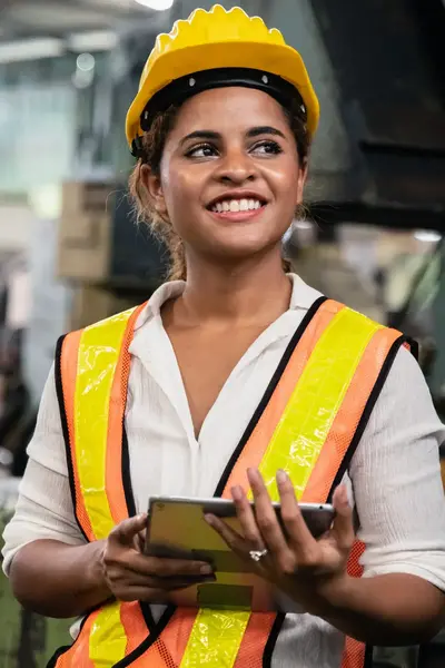 Vrouw in fluorescerend hesje met helm en tablet in fabriek