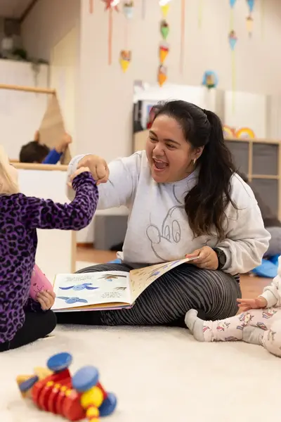 Juffrouw speelt met kleine kinderen op een kleed.