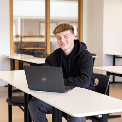 Student in zwarte hoodie achter laptop in klaslokaal