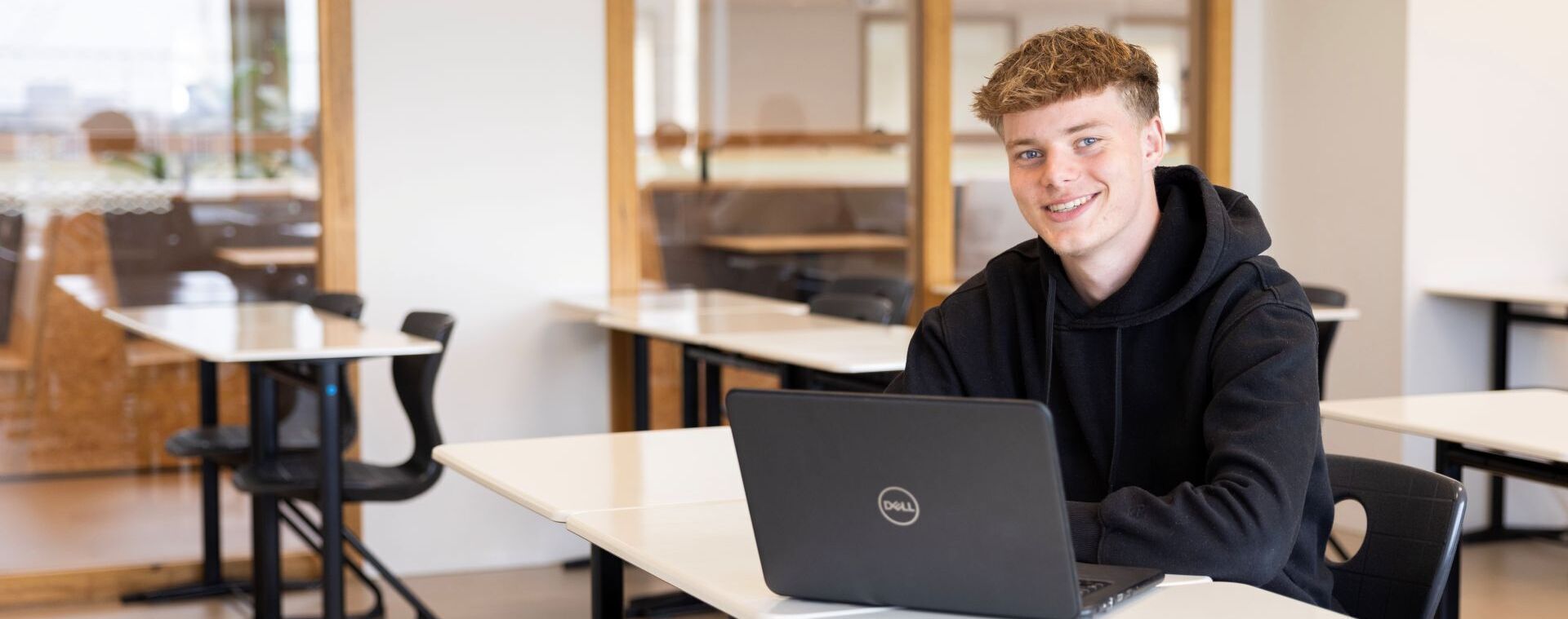 Student in zwarte hoodie achter laptop in klaslokaal
