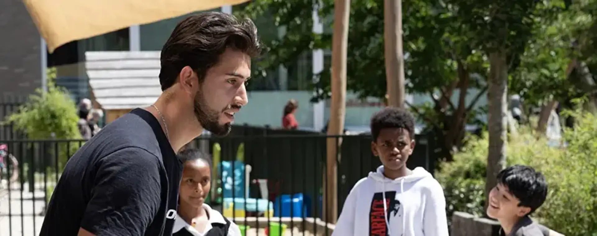 Student speel balspel met kinderen op schoolplein