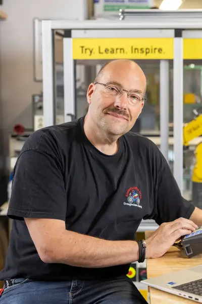 Man met snor tussen elektronische installaties en laptop