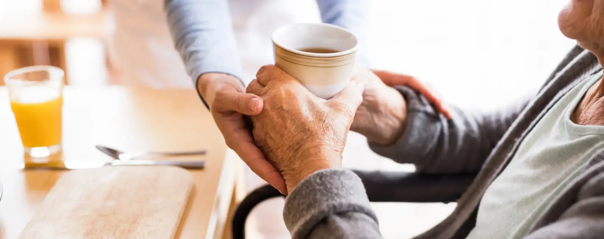 Jonge handen reiken een kop thee aan bejaarde man