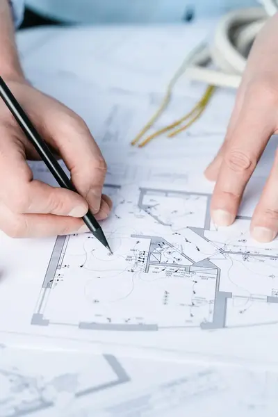 Een technicus tekent nauwkeurig op een bouwtekening, omringd door gereedschap en meetapparatuur, ter voorbereiding op een elektrische installatie.