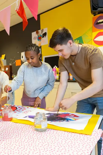 Studenten helpen leerling met verven op basisschool 
