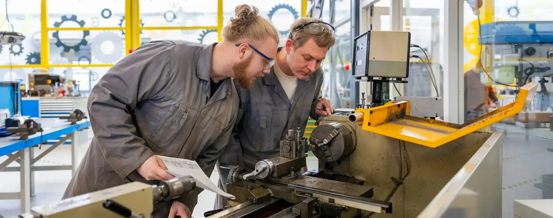 Twee mannen in werkkleding en handleiding buigen zich over machine