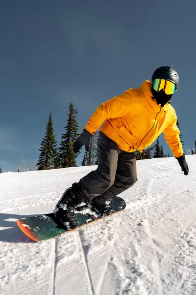 Snowboarder in gele winterjas gaat van helling af. 