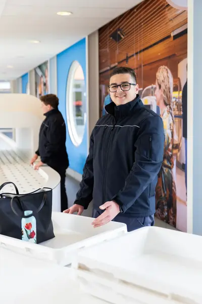 Beveiliger op luchthaven lacht terwijl hij bakken bij de balie klaarzet.