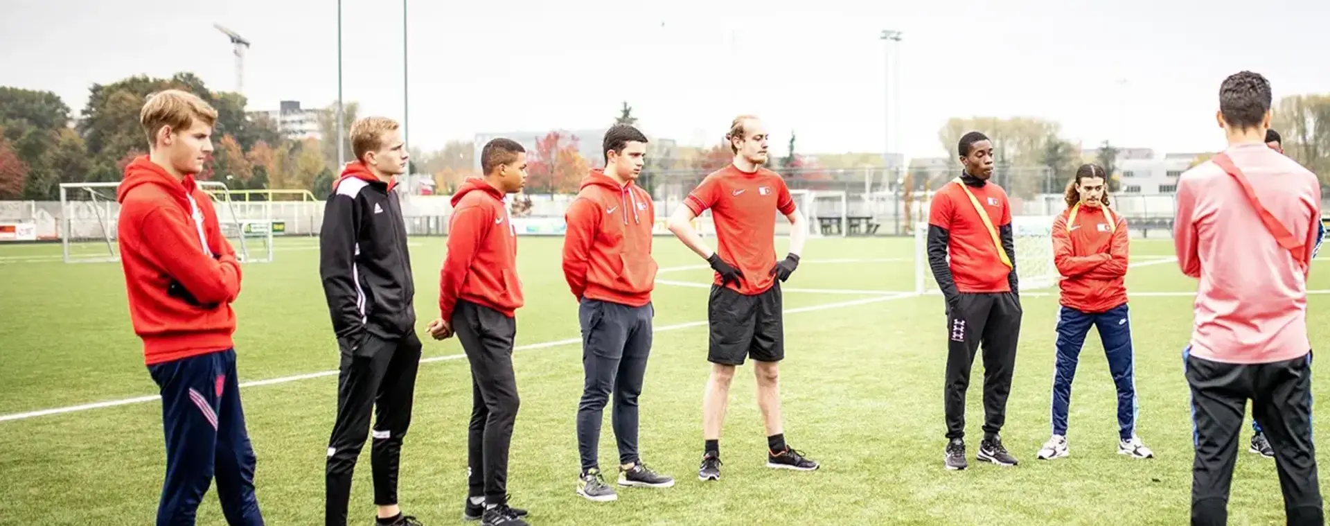 Voetballers staan in een halve cirkel te luisteren naar hun coach