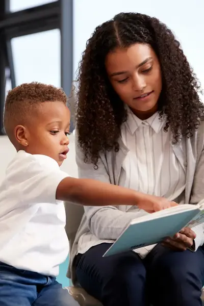 Kind wijst iets aan in boek van docente, terwijl andere kinderen toekijken.