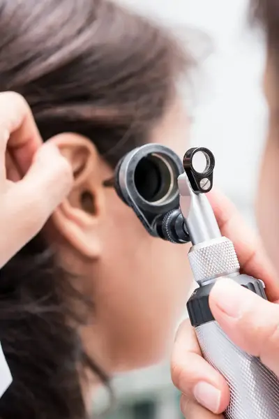 Dokter kijkt in oor patiënt
