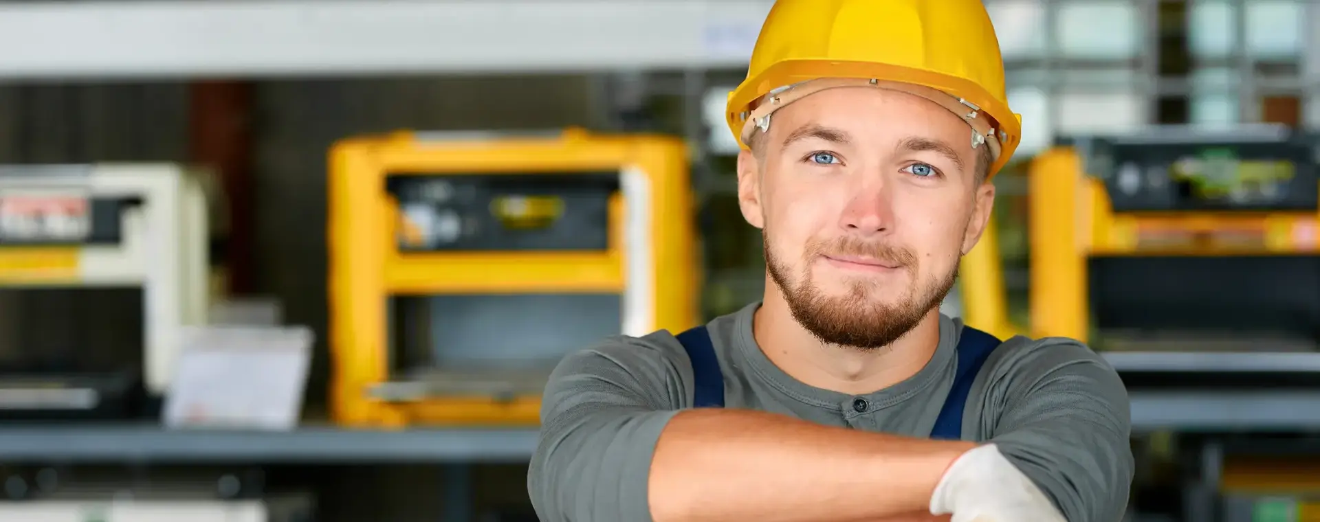 Student met bouwhelm op leunt op machine en lacht in de camera