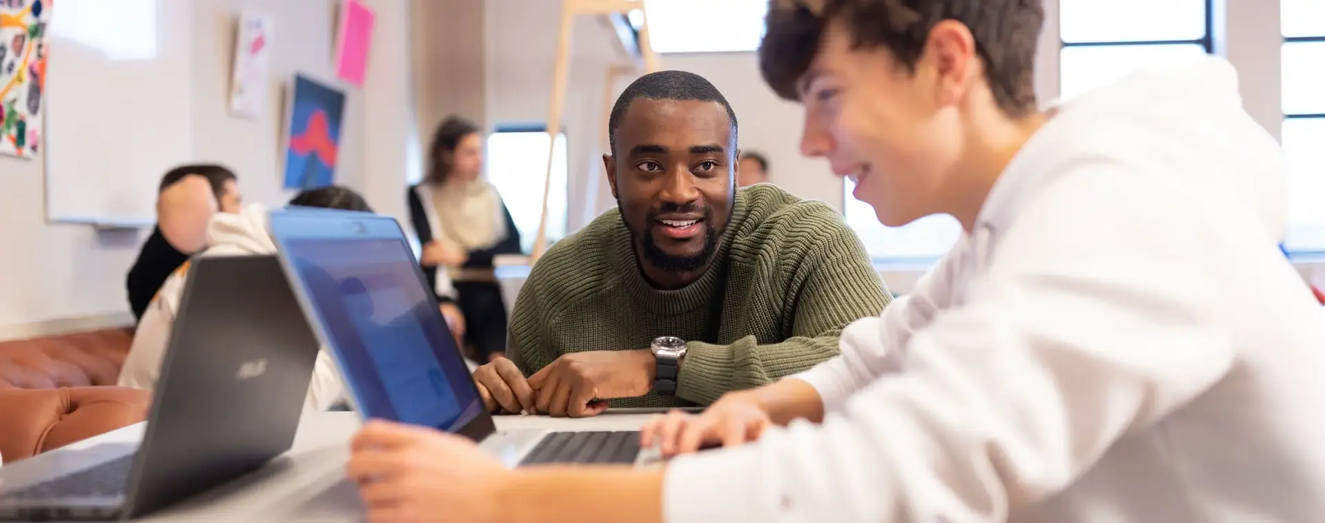 Docent samen met student die achter laptop zit en lacht