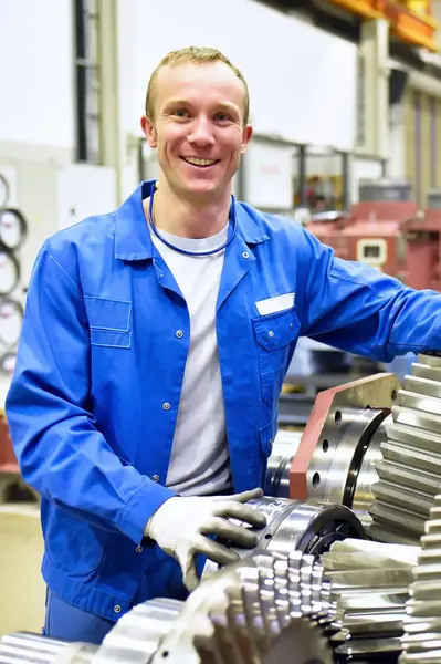 Man in blauwe overall bij tandwielvormige objecten