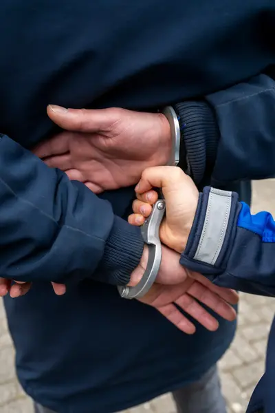 Close-up van handen die in de boeien worden geslagen door handhaver