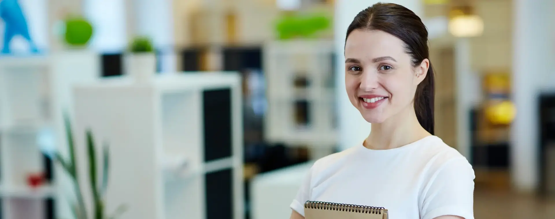 Student kijkt trots in de camera terwijl ze haar schriften omklemt.