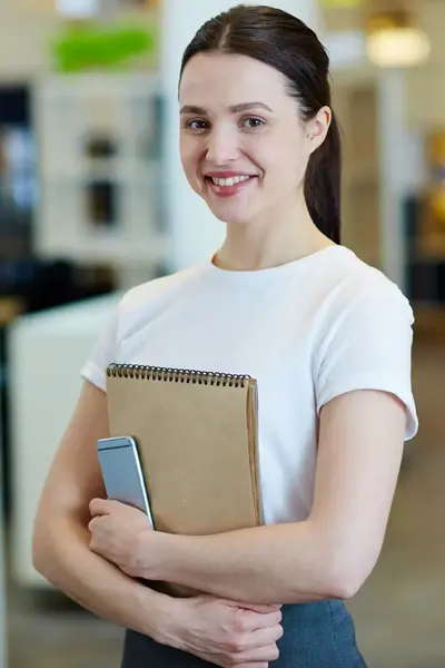 Student kijkt trots in de camera terwijl ze haar schriften omklemt.