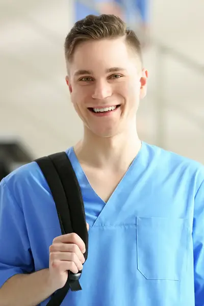 Verpleger in uniform glimlacht naar de camera met collega's op de achtergrond