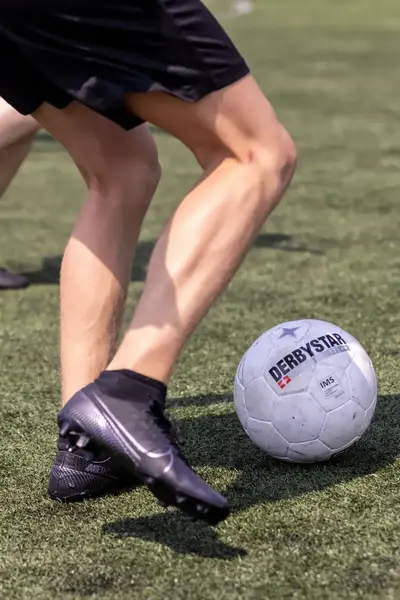 Benen trappen tegen een voetbal op een voetbalveld.