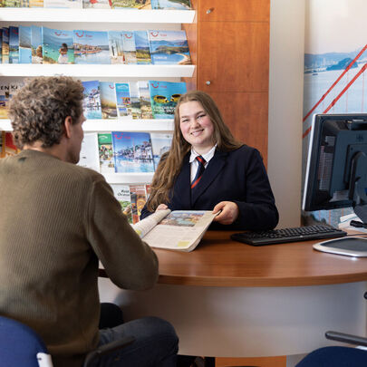 Student Toerisme en Hospitality toont reisbrochure aan klant in reisbureau