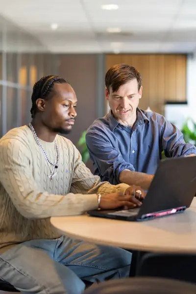 Twee mannen achter laptop aan een ronde tafel.